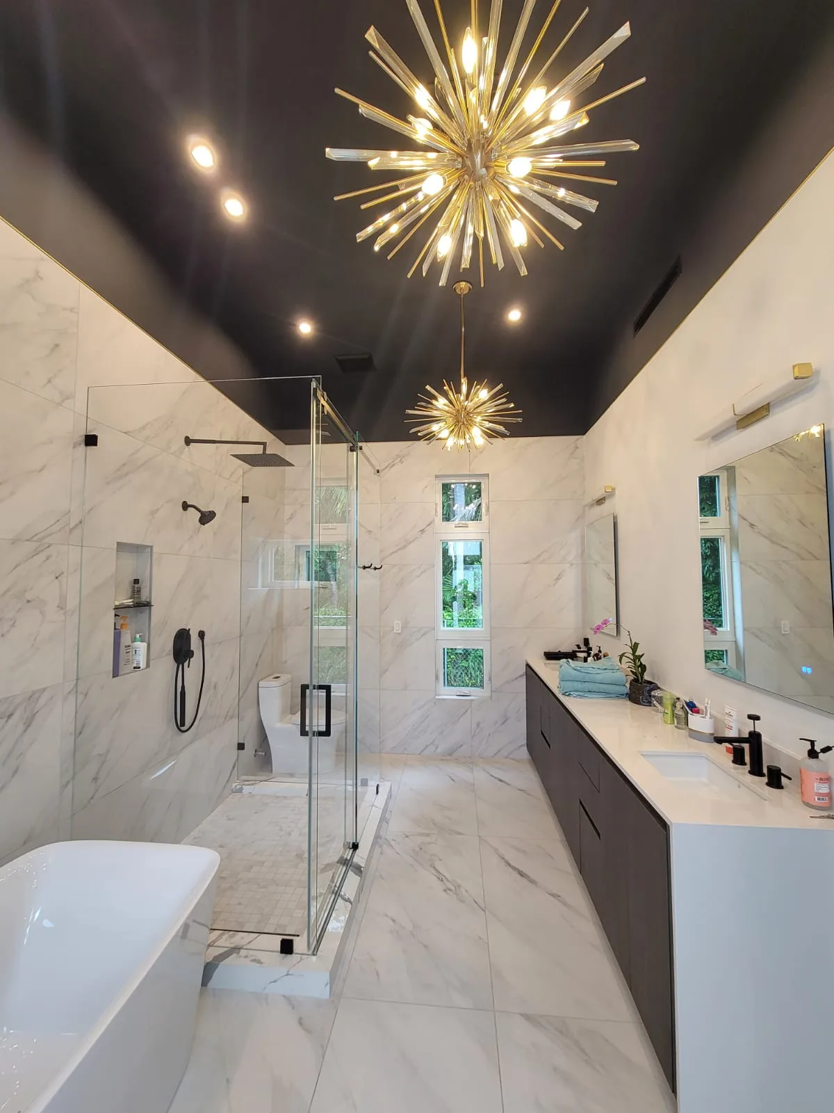 Moody Brickell master bathroom with calacatta walls, freestanding tub, and sputnik chandeliers