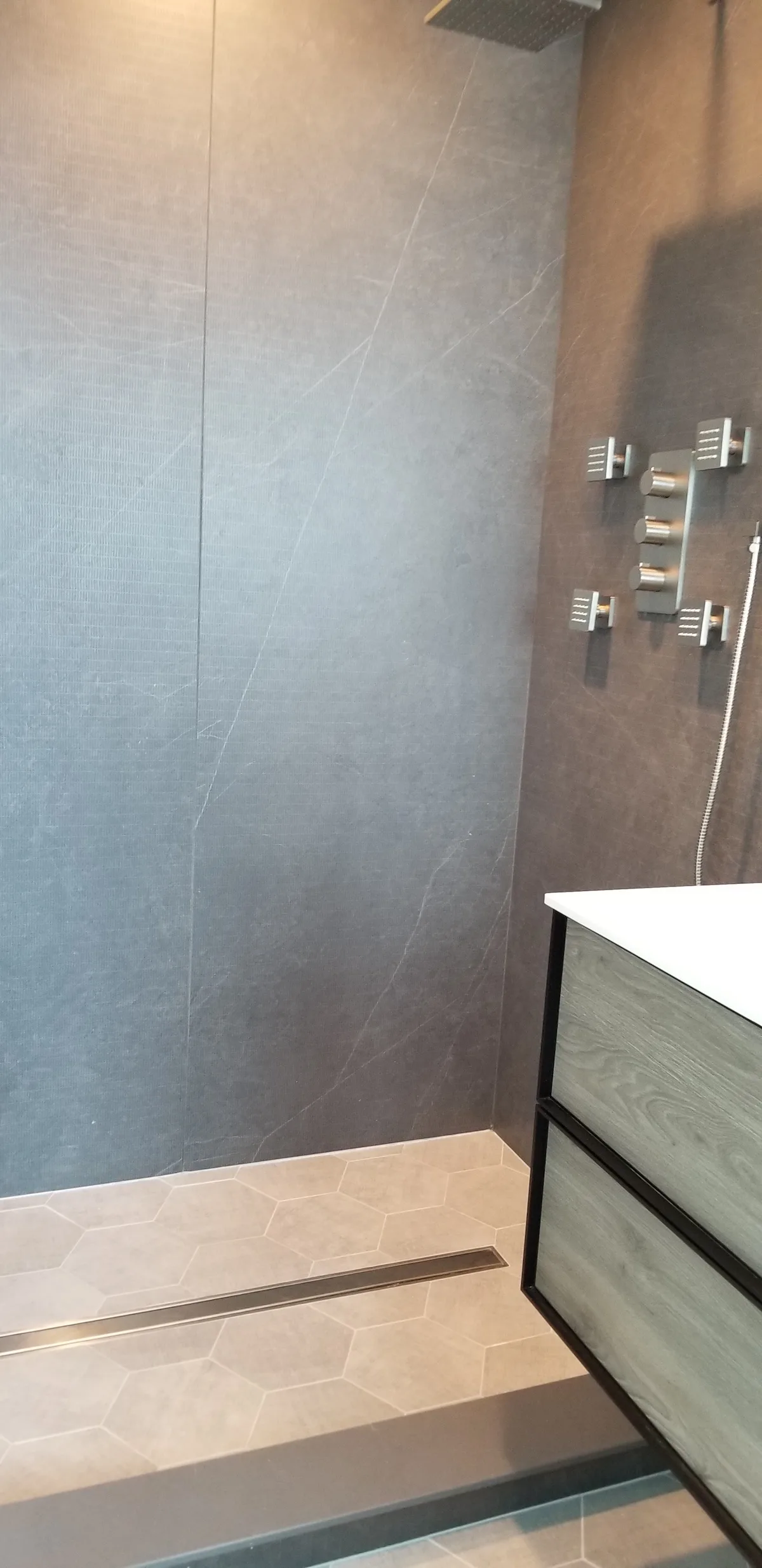 Linear shower drain set into hexagonal floor tile against a moody dark slab wall in a Pinecrest bathroom